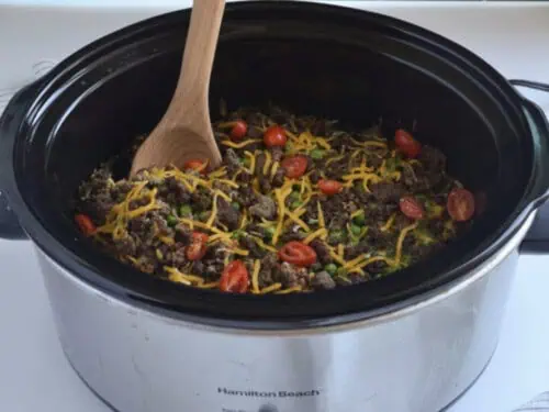 seven layer casserole in a crock pot, with a wooden spoon.